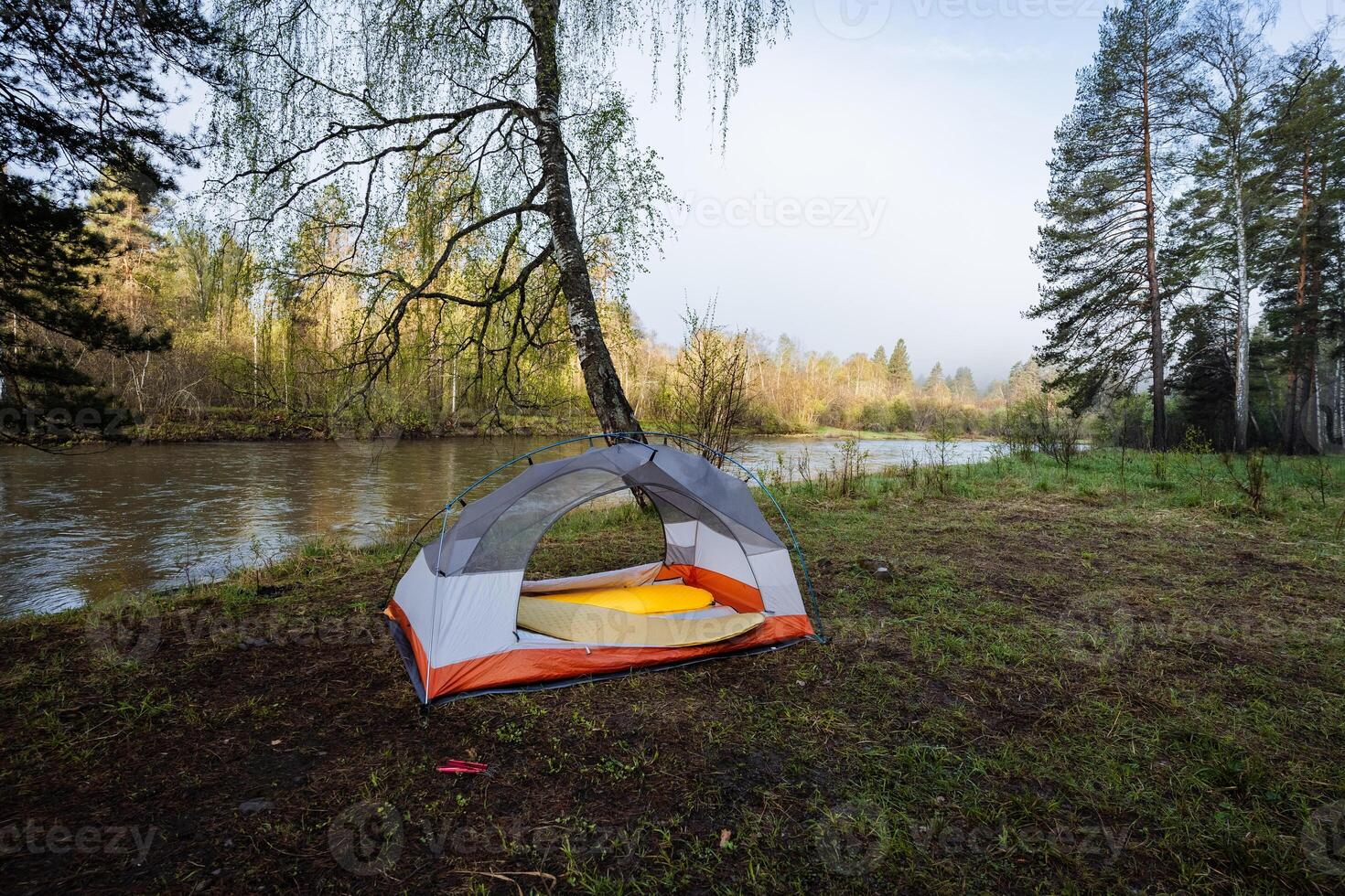 A tranquil and serene riverside camping scene featuring a cozy tent nestled under expansive, clear blue skies that invite adventure and exploration in the great outdoors on a beautiful summer morning photo