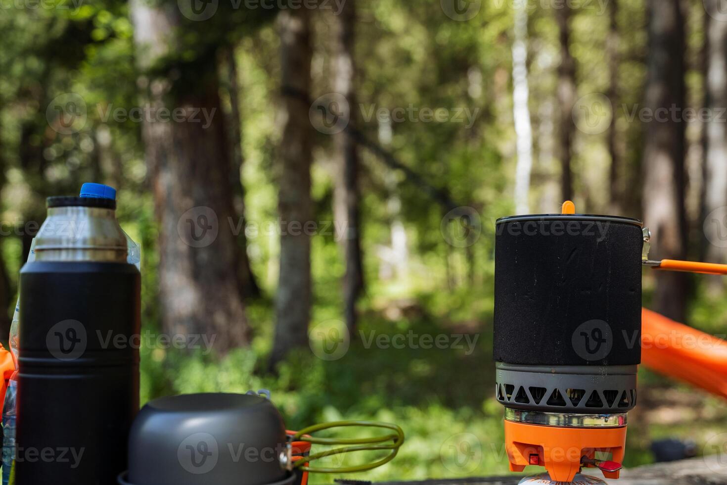 A portable camping stove is strategically placed on a rustic wooden table that is set within the serene woods, surrounded by lush nature and the soothing sounds of wildlife all around photo
