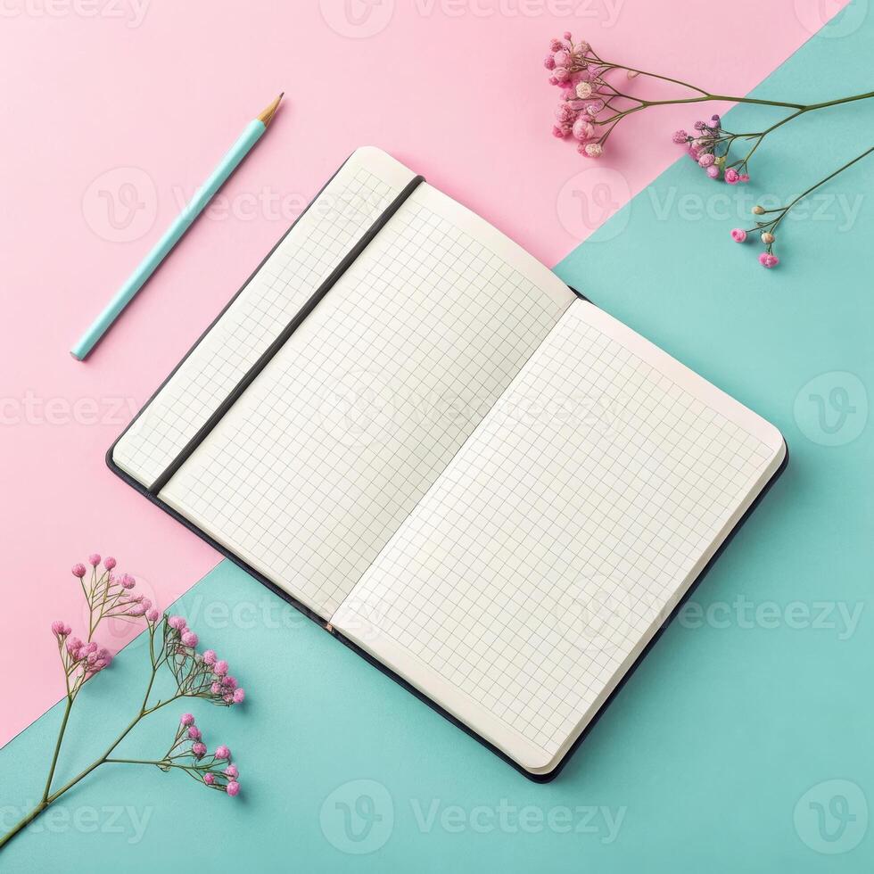 Open notebook with grid pages on pastel pink and blue background with flowers and pencil in vibrant arrangement and copy space photo