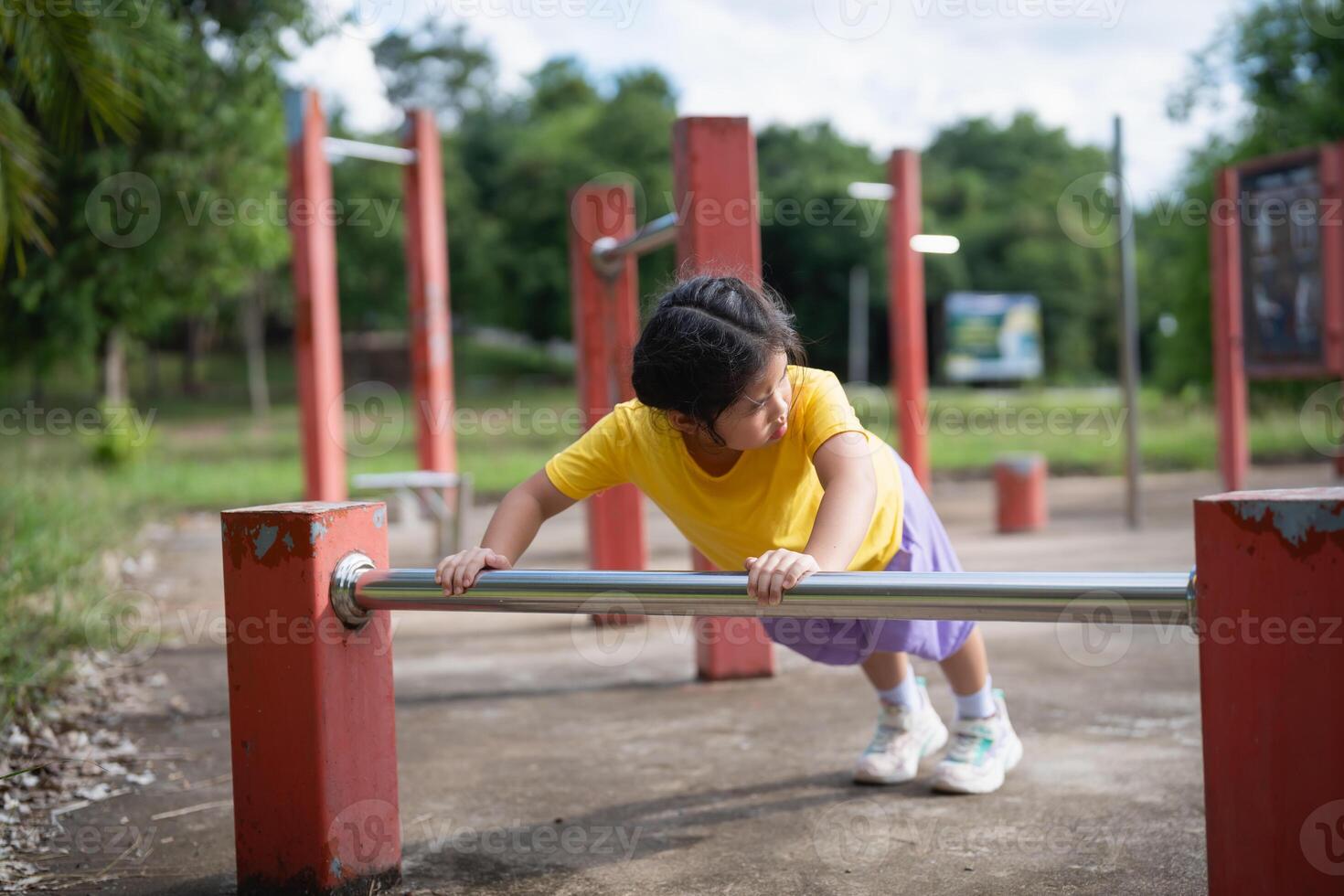 Asian Young girl exercising outdoors on a playground using a fitness bar to strengthen her body and promote health in a vibrant green environment photo