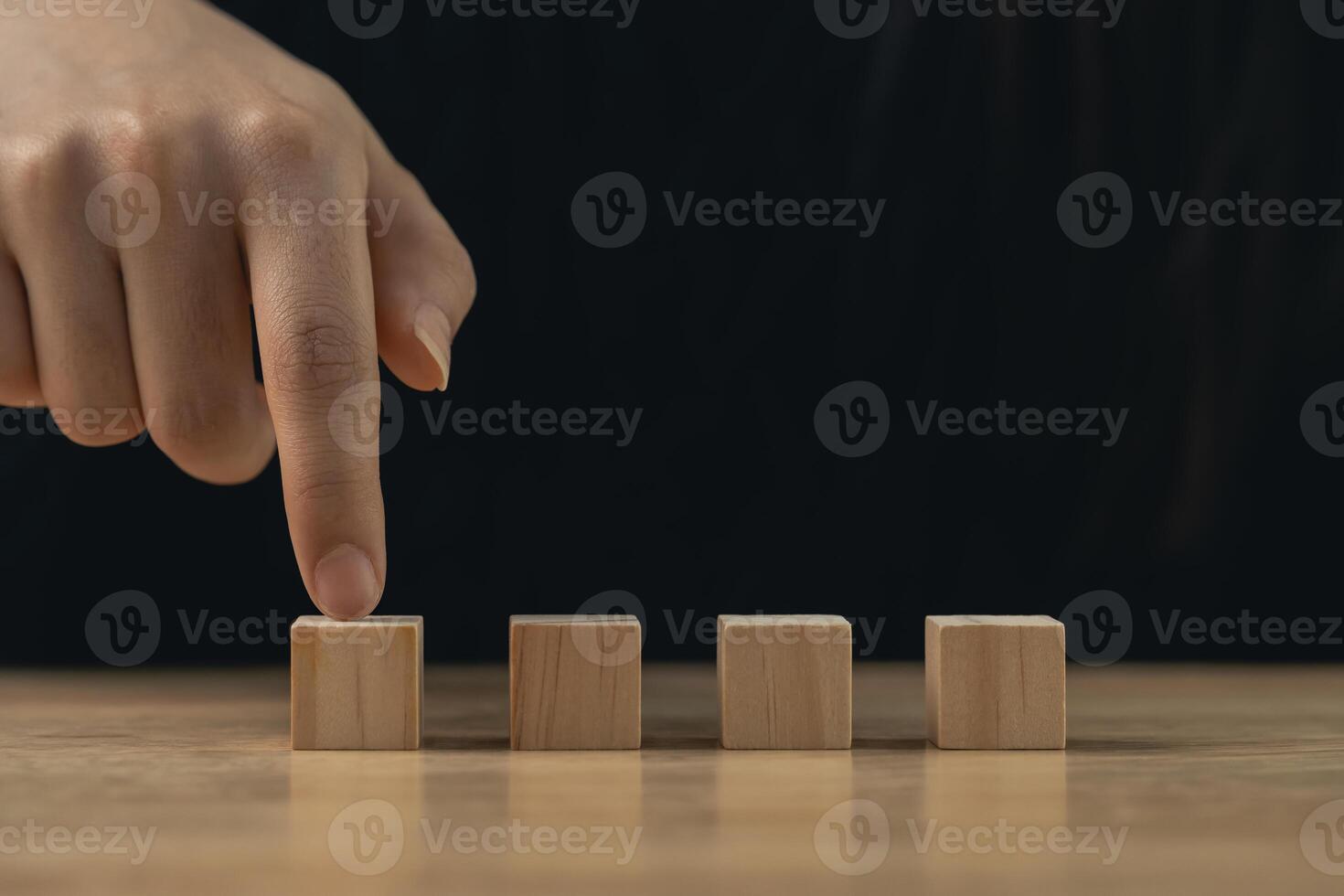 Close-up of Hand Pointing at Wood Blocks on Table with Dark Background, Concept of Choice, Decision Making, and Creativity in Idea Generation Process photo