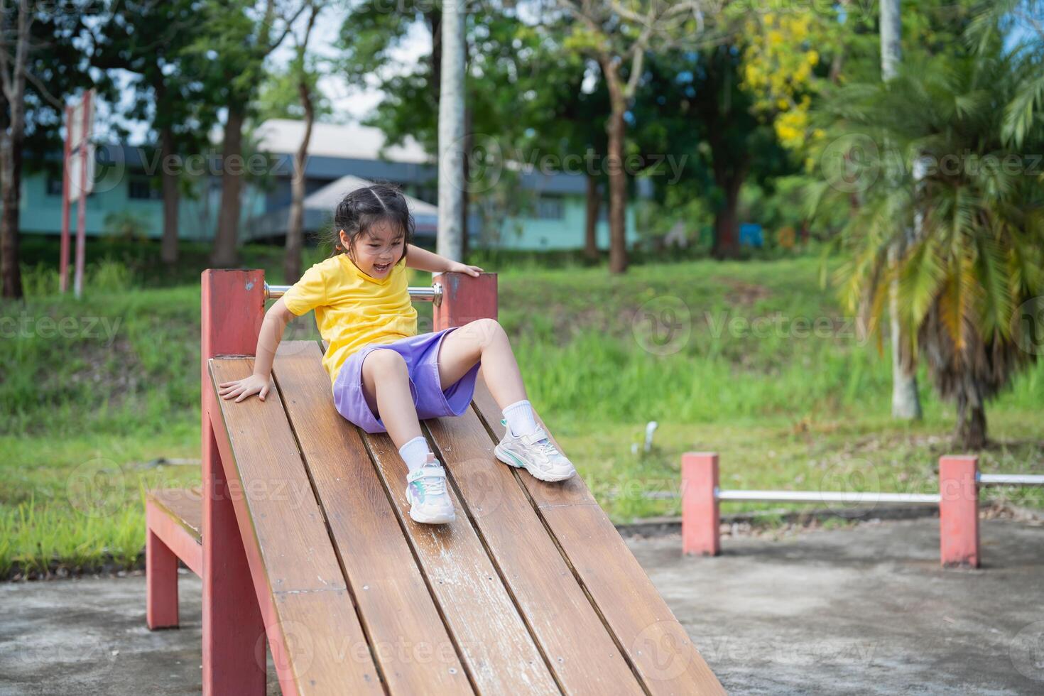 Asian Young child enjoying a sunny day at the playground, sliding down a wooden play structure, laughter and joy captured in outdoor playtime fun photo