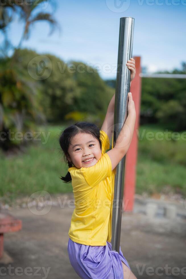 Joyful Asian child playing on a shiny metal pole in a vibrant outdoor playground, showing happiness and lively energy in a sunny environment photo