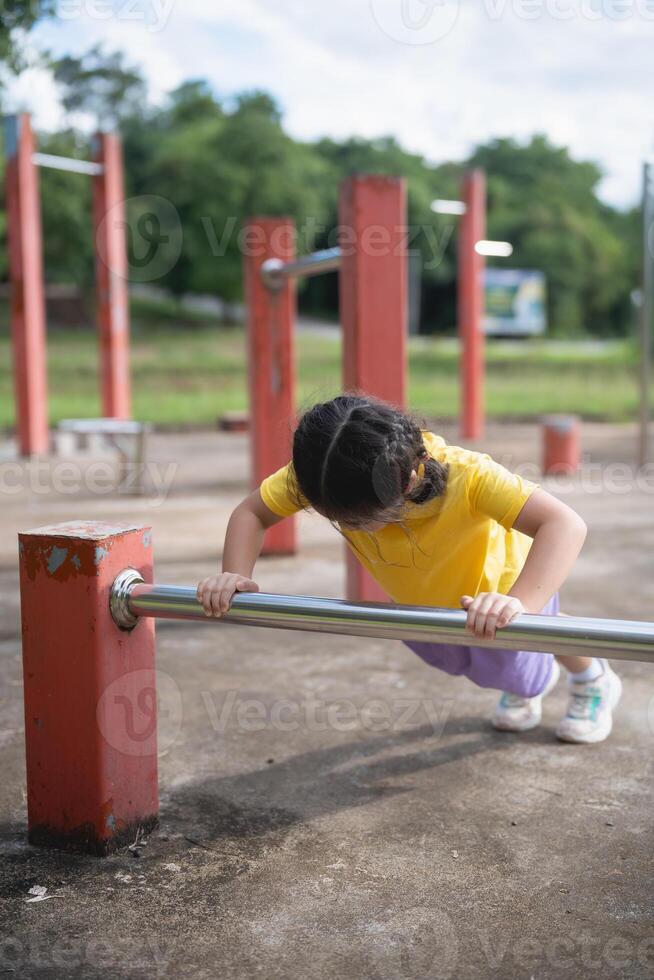 Asian Young Girl Performing Push-Ups in Outdoor Playground, Enhancing Strength and Fitness in Natural Environment During Daylight Hours photo