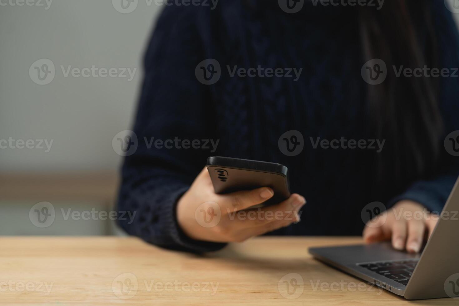 Person using smartphone and laptop on wooden table with cozy atmosphere for remote work or digital communication concept photo