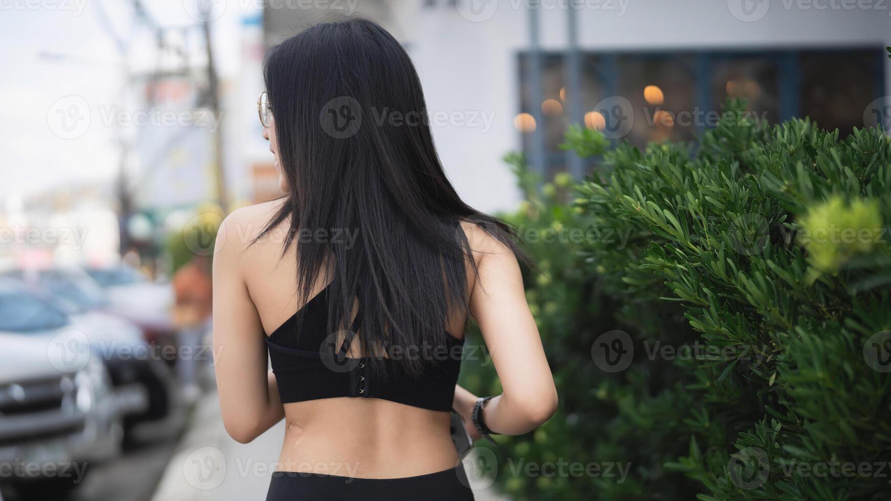Young woman with long dark hair walking along a street in urban setting, wearing black outfit and showcasing a relaxed lifestyle in a vibrant city environment photo