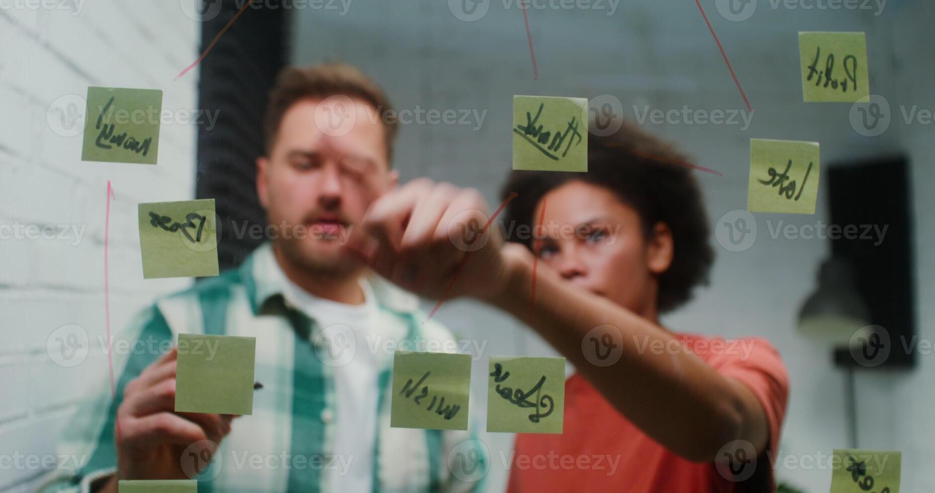 A man and woman pointing at sticky notes on a wall photo