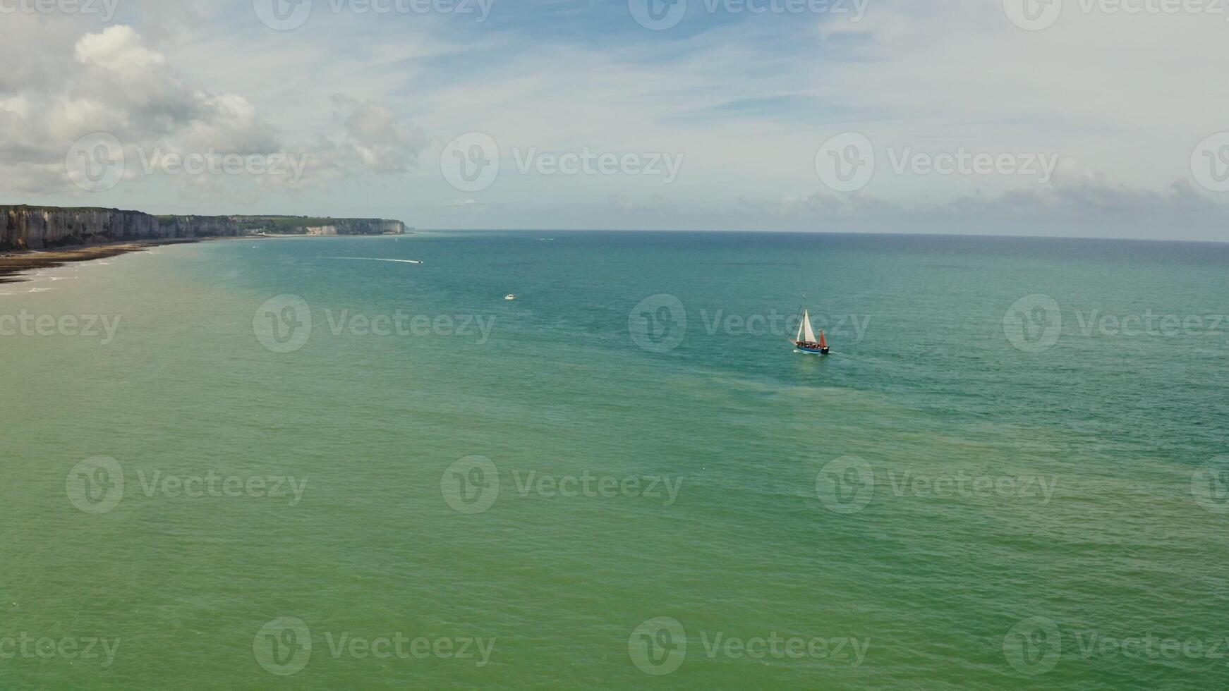 A sailboat is sailing in the ocean near a beach photo