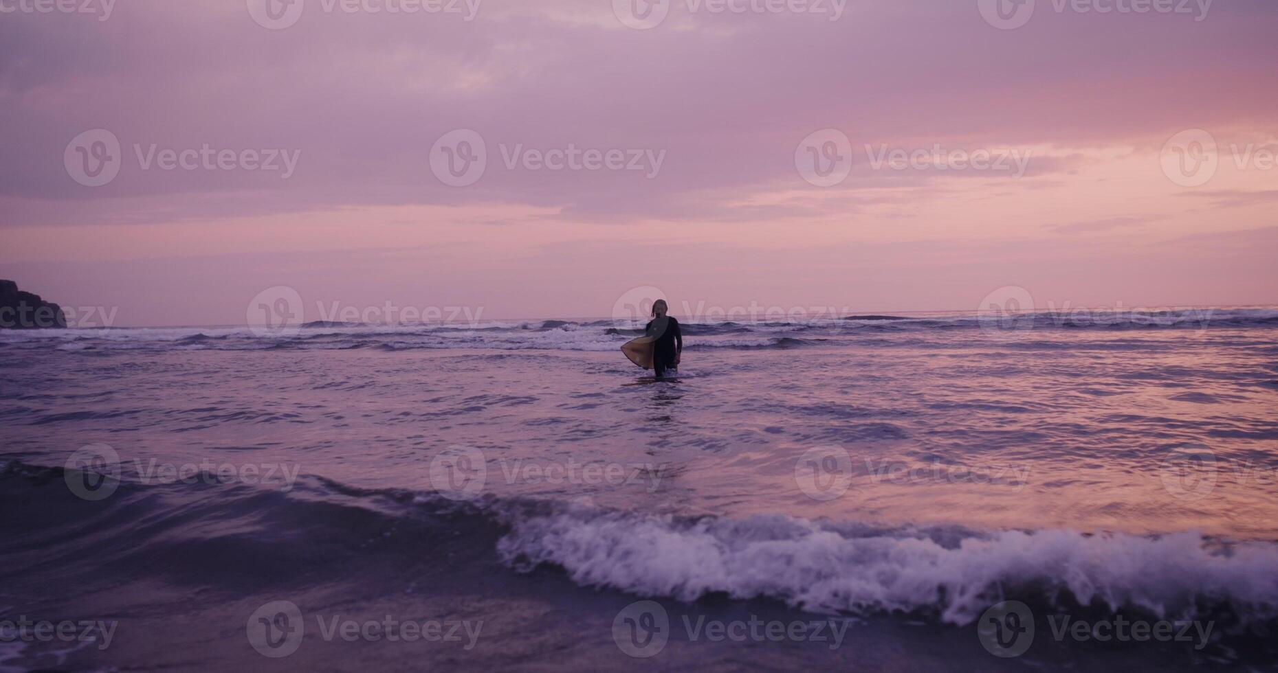 A person standing in the water with a surfboard photo