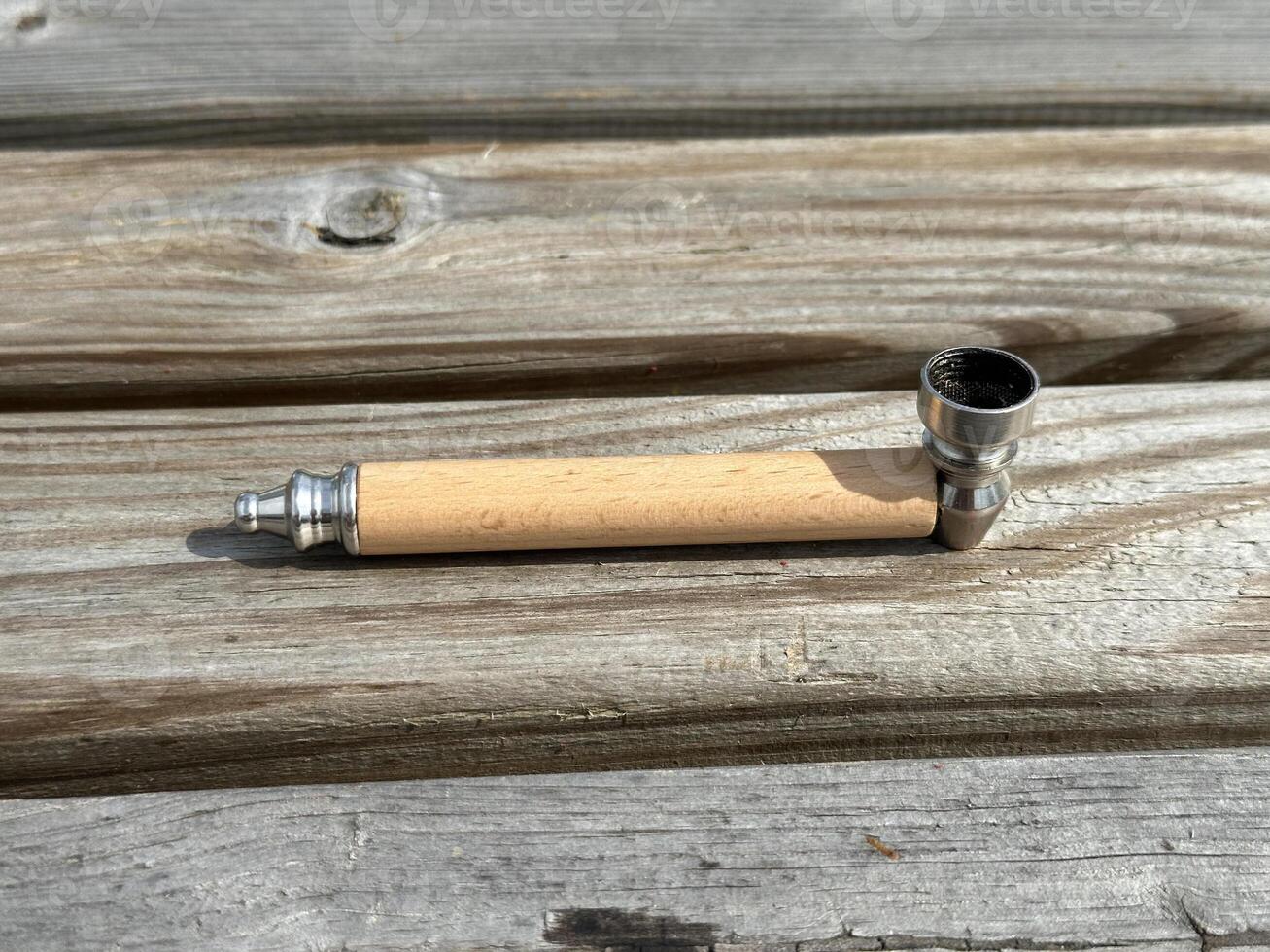 Wooden smoking pipe with metal bowl resting on rustic wooden surface, showcasing craftsmanship and natural materials in a serene setting photo