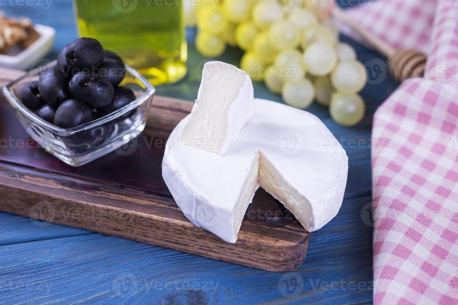 appetizer camembert cheese with olives on a wooden board with honey and grapes on a blue background photo
