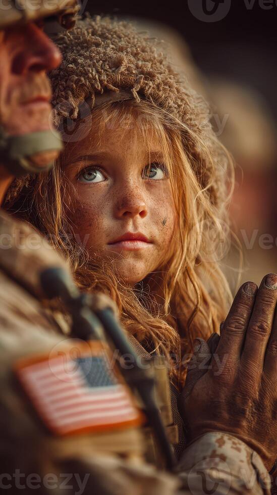 Young girl gazing up intently while standing beside a soldier outdoors during sunset in a military setting photo