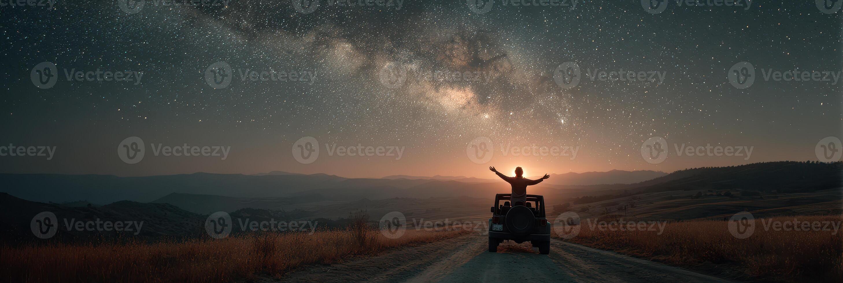 Stargazer celebrates the beauty of the Milky Way from a mountaintop road at dusk with arms raised in awe and wonder photo