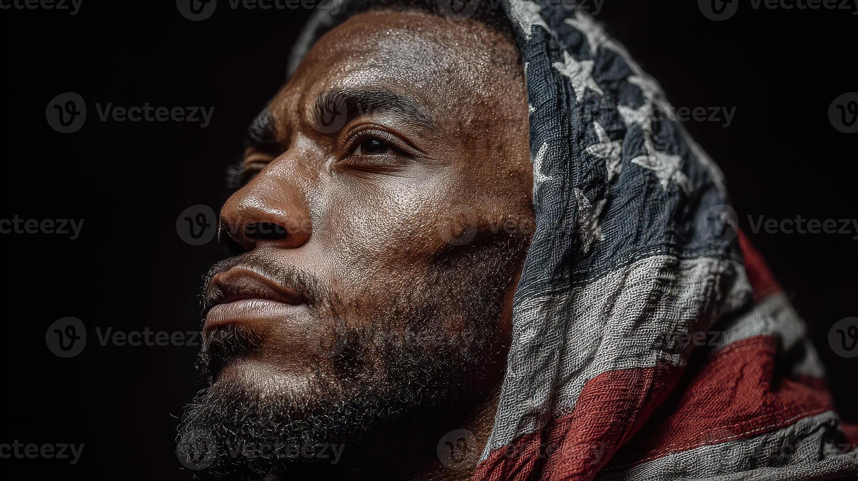 Man wearing American flag draped on head gazes thoughtfully against a dark background in a moment of reflection photo