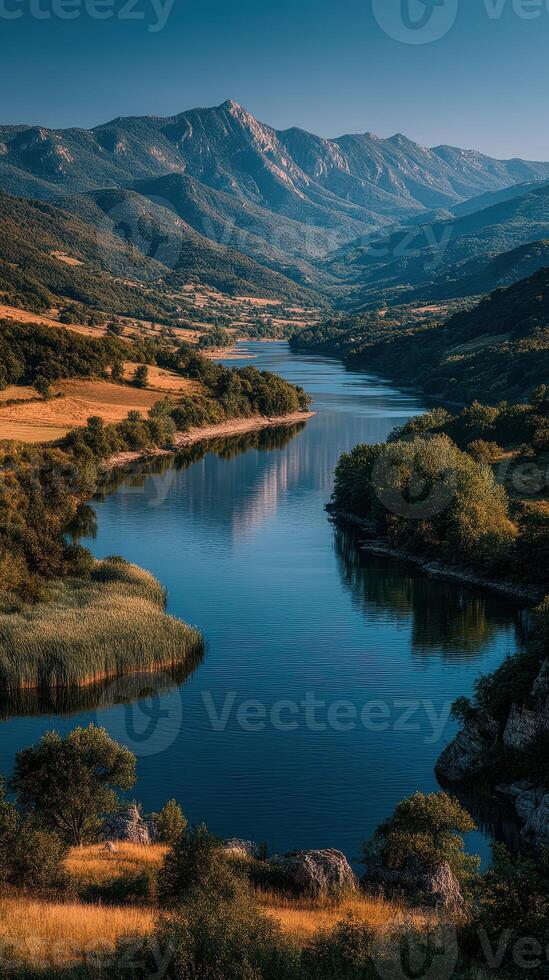 Scenic river meandering through lush valleys under a clear blue sky in the mountains at sunset photo
