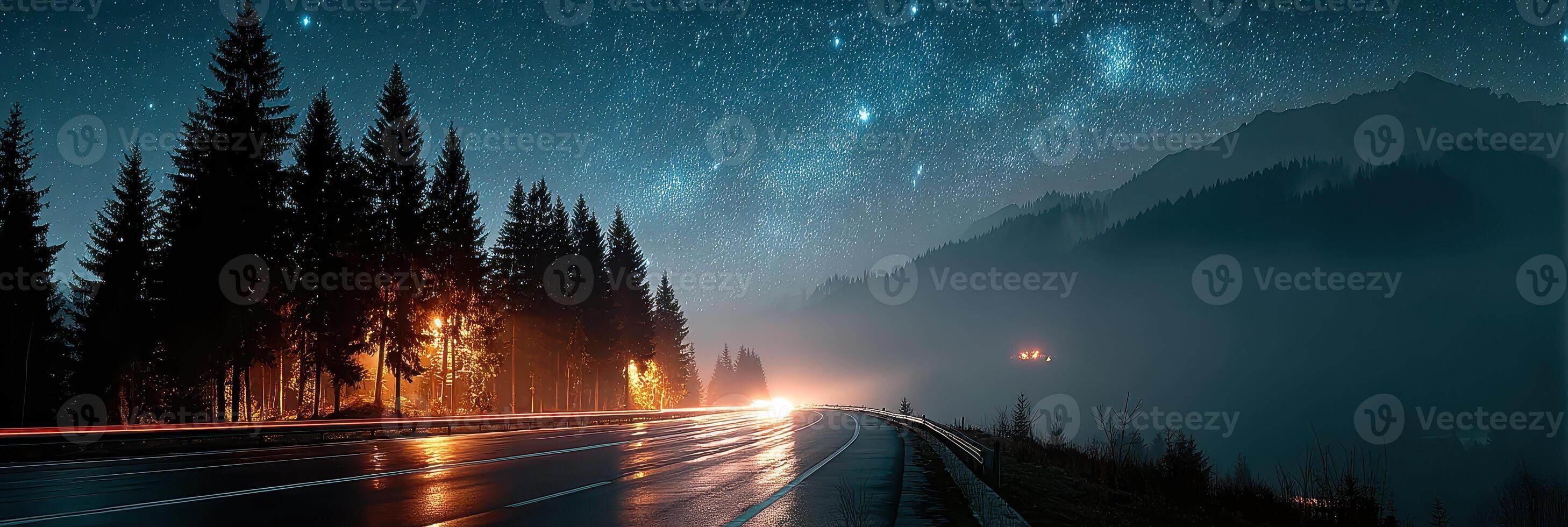 Starry night over a winding road in the mountains with glowing lights and misty trees photo