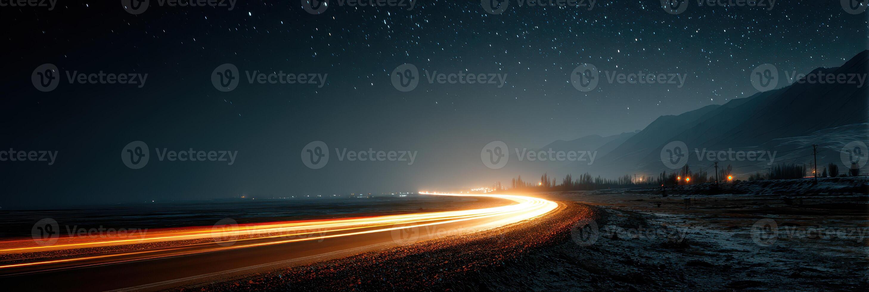 Nighttime coastal road with illuminated car trails under a starry sky near mountains photo