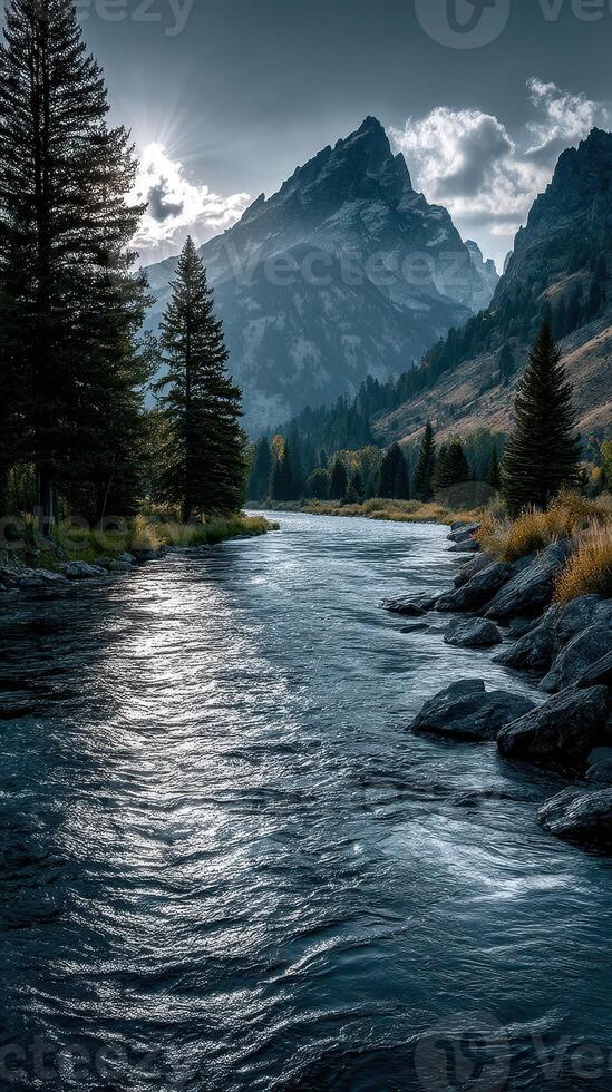 Tranquil river flows through mountain valley at sunset with towering peaks and dense trees photo