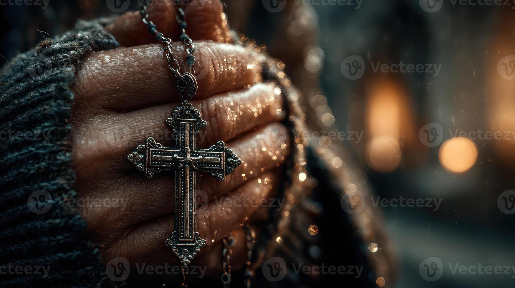 Hands holding a silver cross pendant while praying in a dark and moody setting with warm light in the background photo