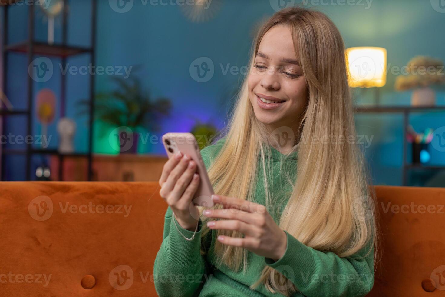 Caucasian young woman sitting on sofa, using smartphone share messages on social media application photo