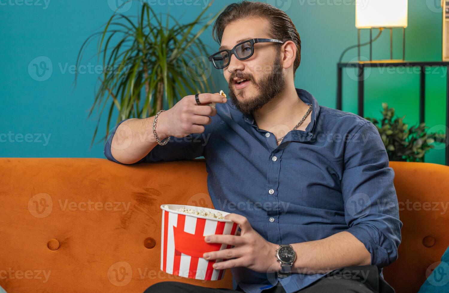 Lebanese man sits on sofa eating popcorn, watching interesting TV serial, sport game online at home photo