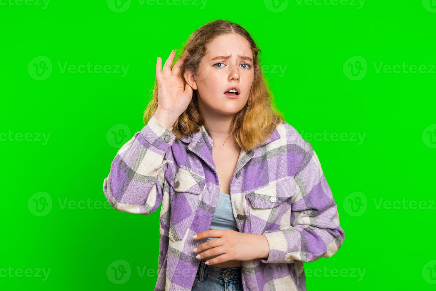 Young woman trying hear you looking confused and frowning, keeping arm near ear for louder voice photo