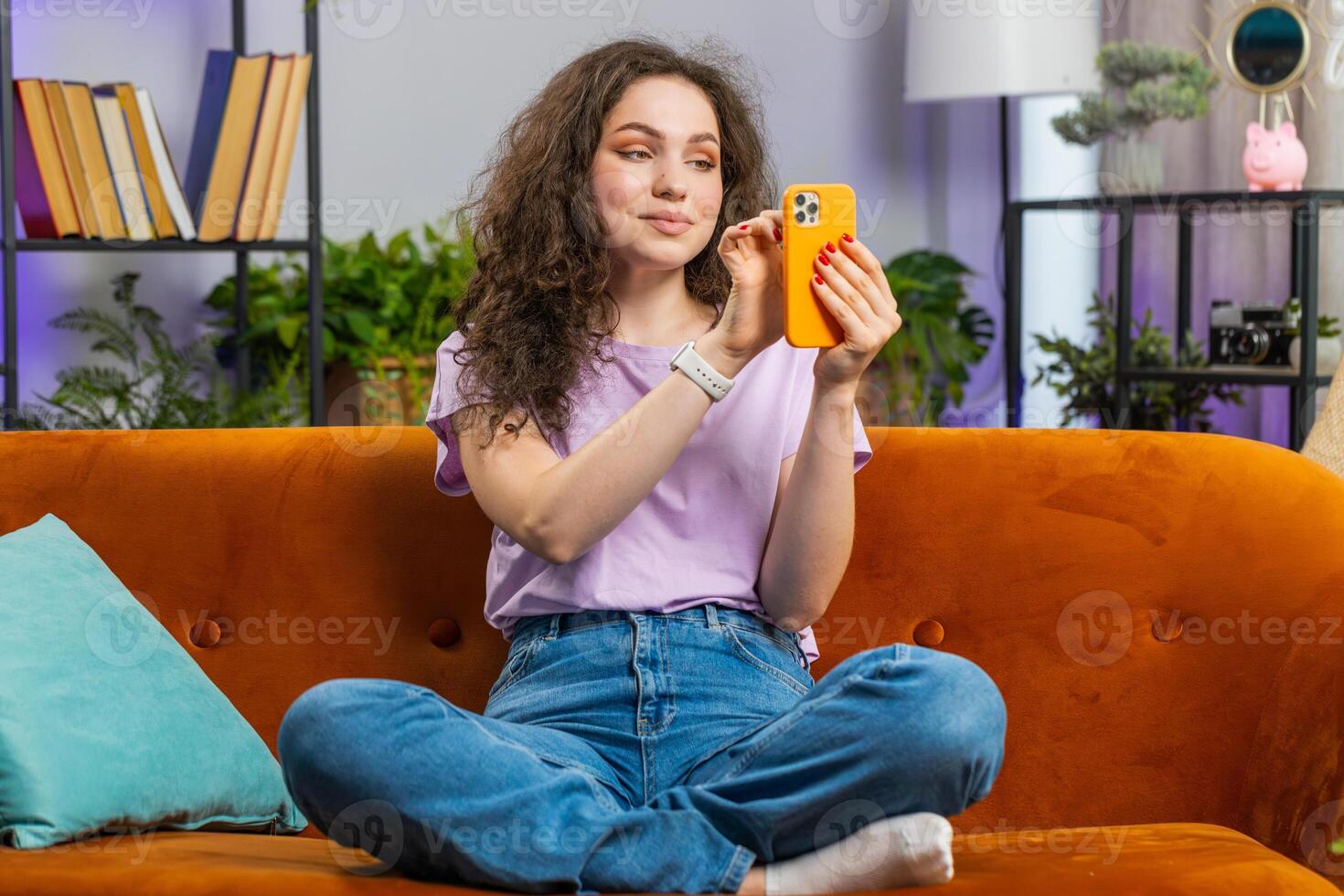 Woman sitting on sofa using smartphone share messages on social media application watching movies photo