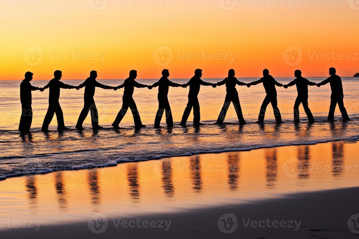 Silhouette of people linked hands, walking along shoreline at sunset photo