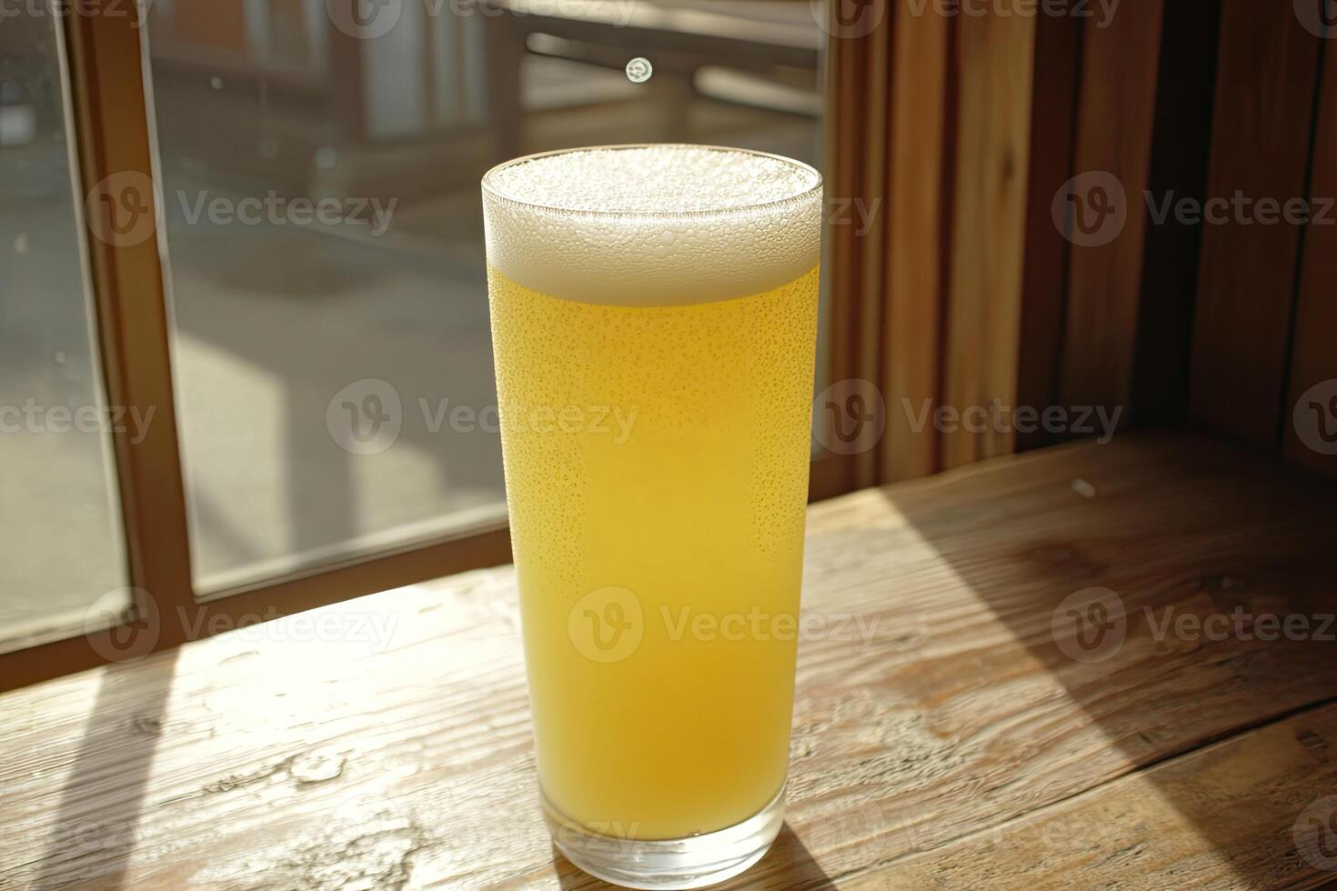 Light, golden-yellow beer in tall glass, frothy top, sunlight through window photo