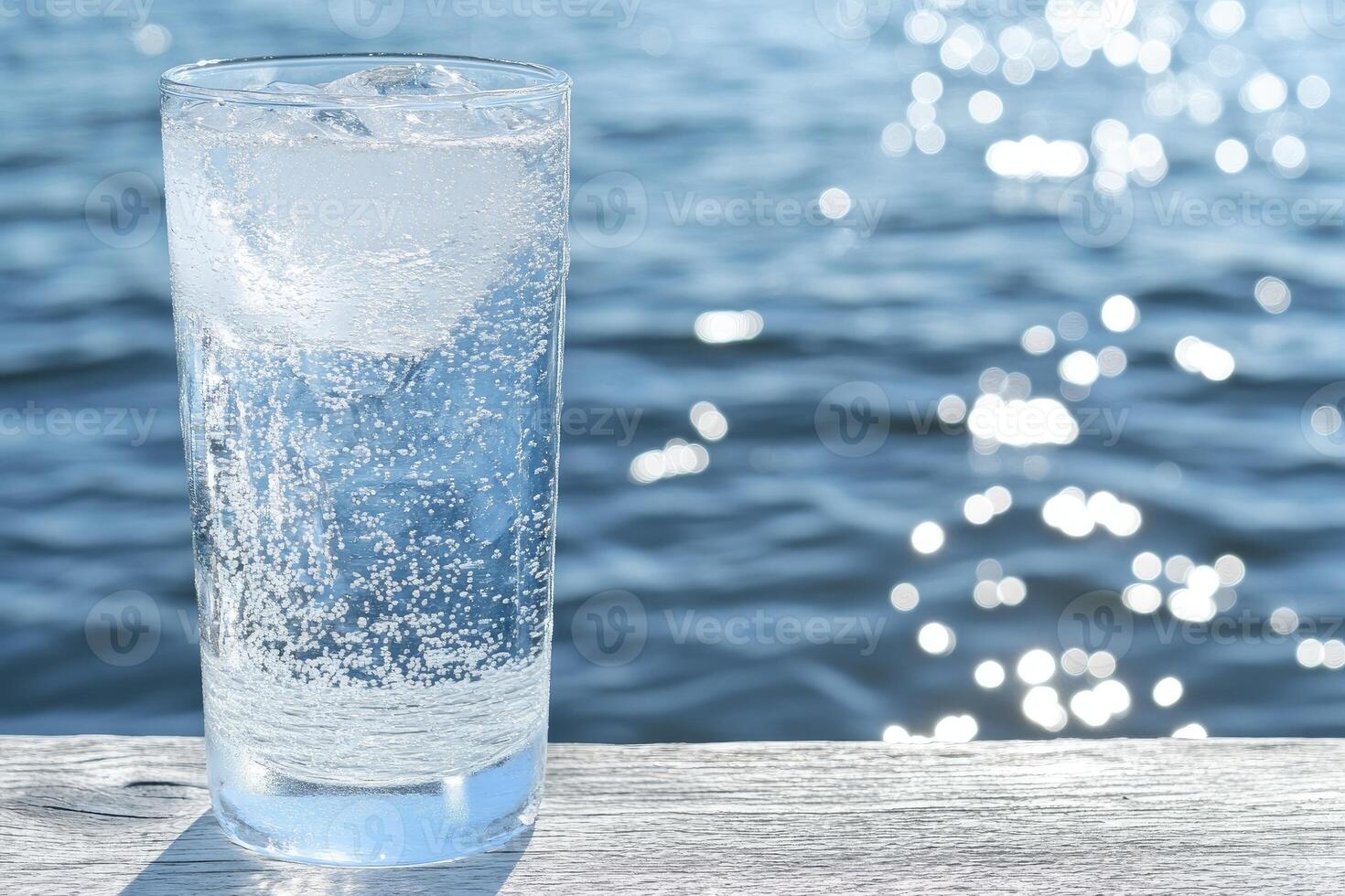 Refreshing glass of sparkling water with ice, ocean backdrop photo