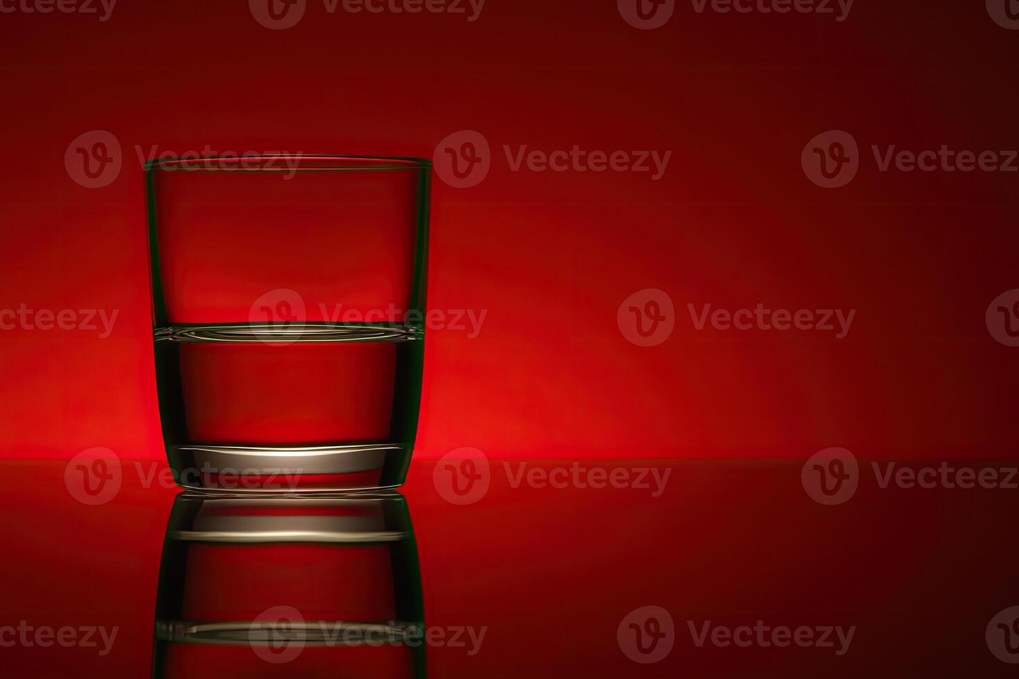 Half-full glass of water against a red backdrop photo