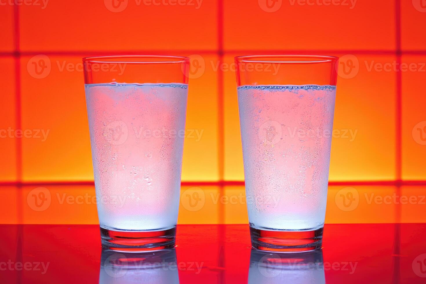 Two glasses of iced water against a vibrant orange background photo