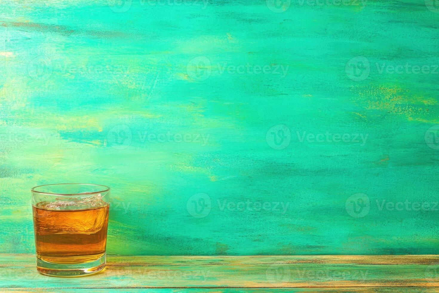A glass of amber liquid with ice on a teal background photo