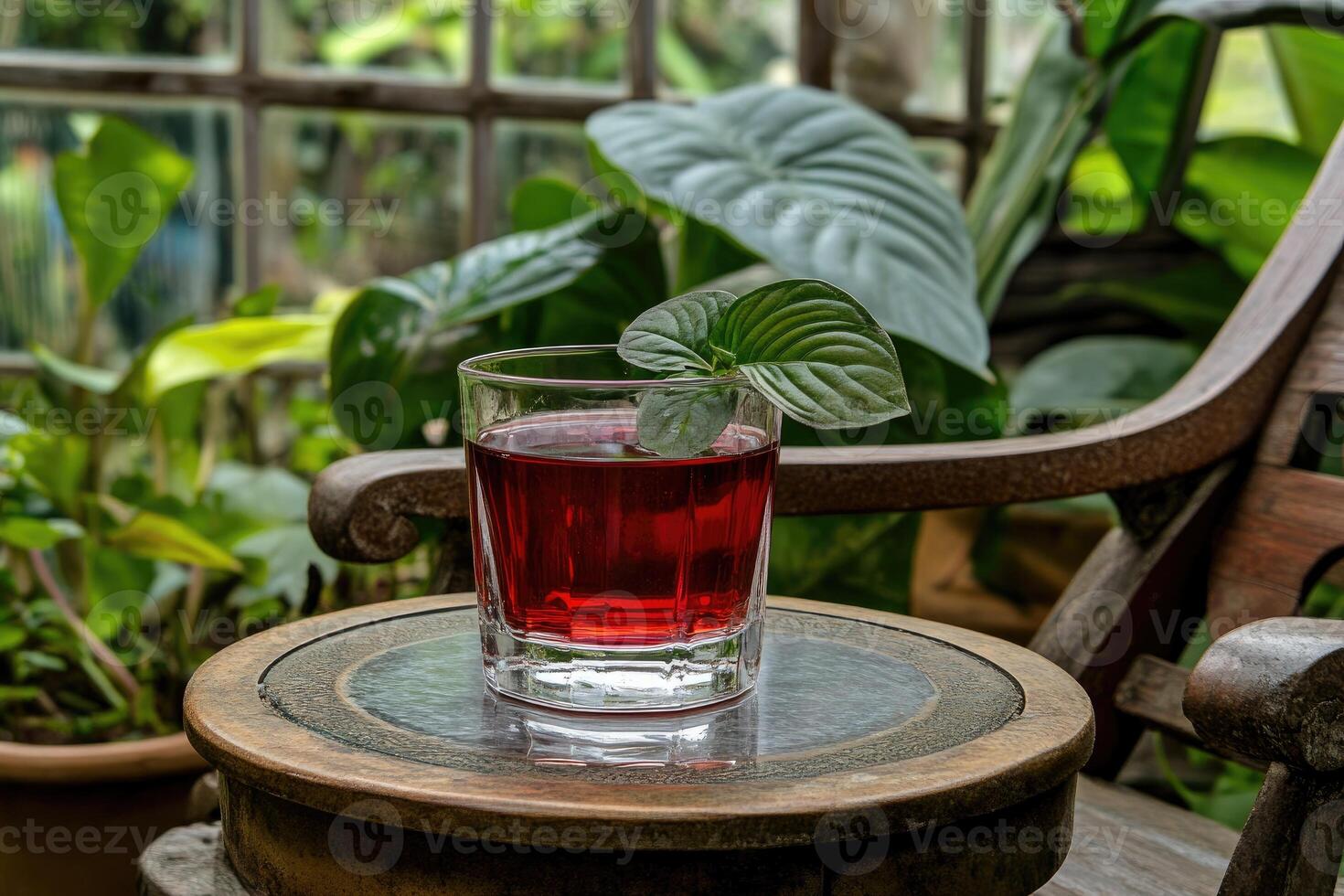 Red drink in glass on wooden table amidst plants photo