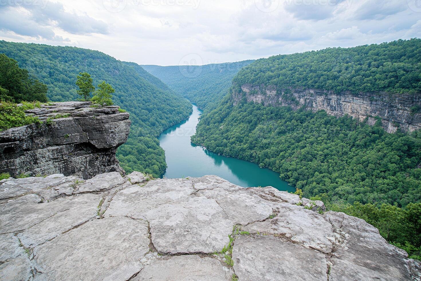 High viewpoint over a serene river valley. Lush green hills surround a winding, deep blue river, nestled within a dramatic canyon. Rocky outcrop offers a panoramic vista photo