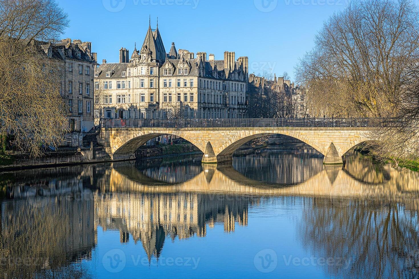 Picturesque stone bridge over calm river, reflecting historic buildings photo