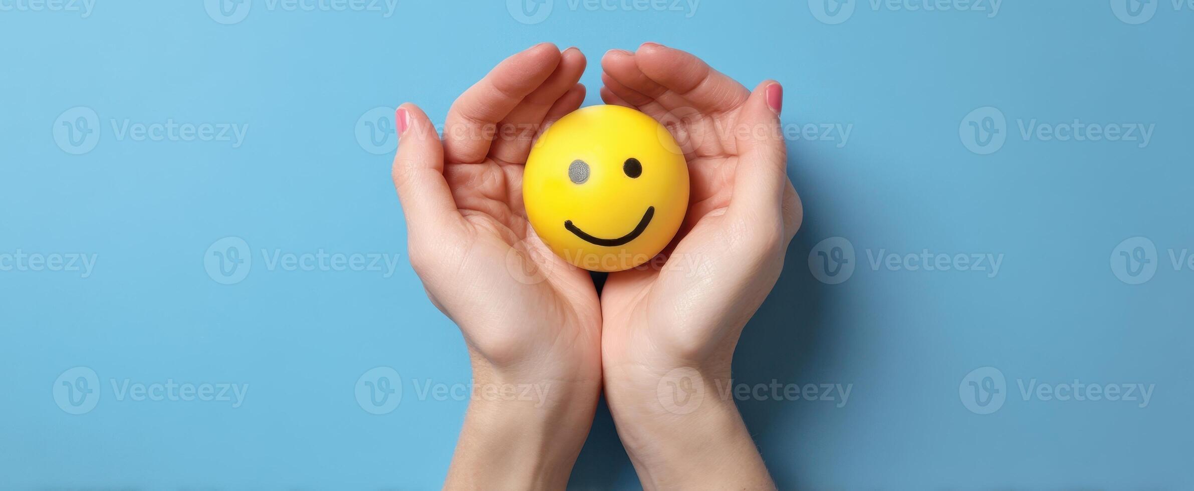 The cheerful yellow smiley ball cradled in caring hands against a blue background. photo