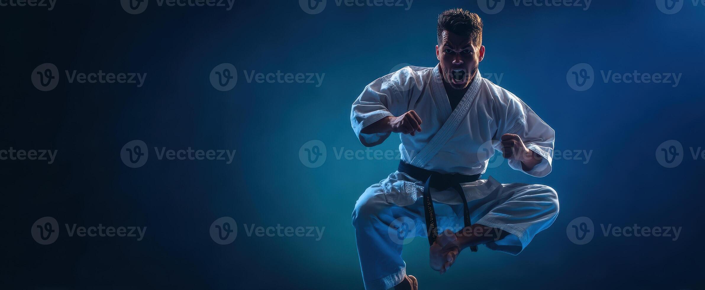 The karate practitioner executing a powerful jumping kick against a dramatic blue backdrop. photo