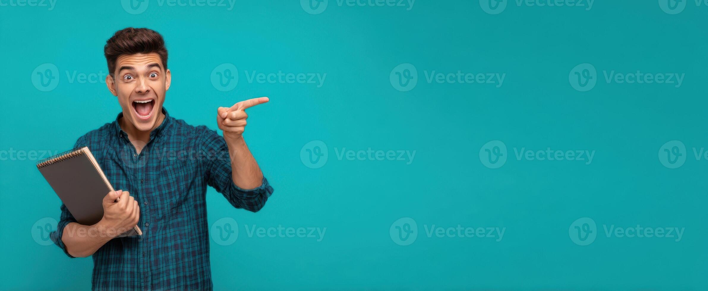 The enthusiastic man pointing while holding a notebook on a vibrant blue background. photo
