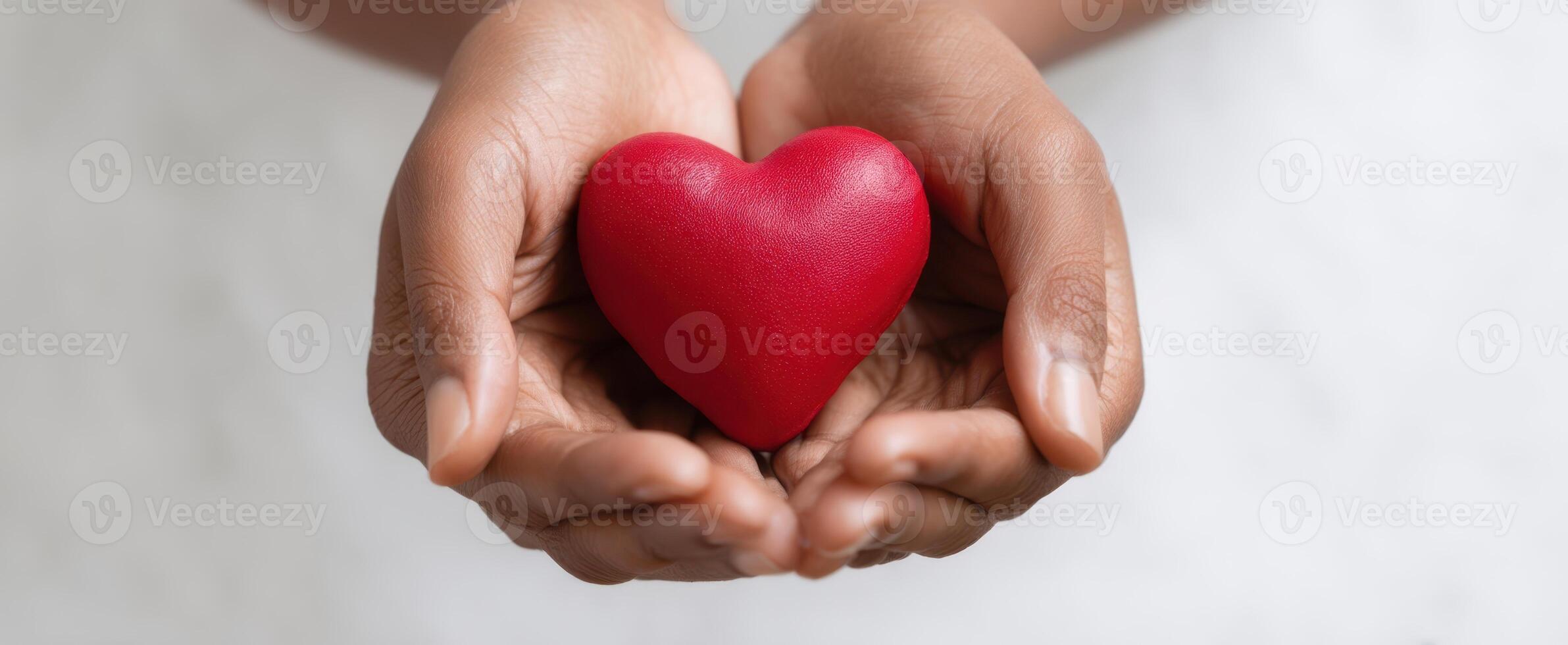 The hands gently holding a vibrant red heart symbolizing love and compassion. photo
