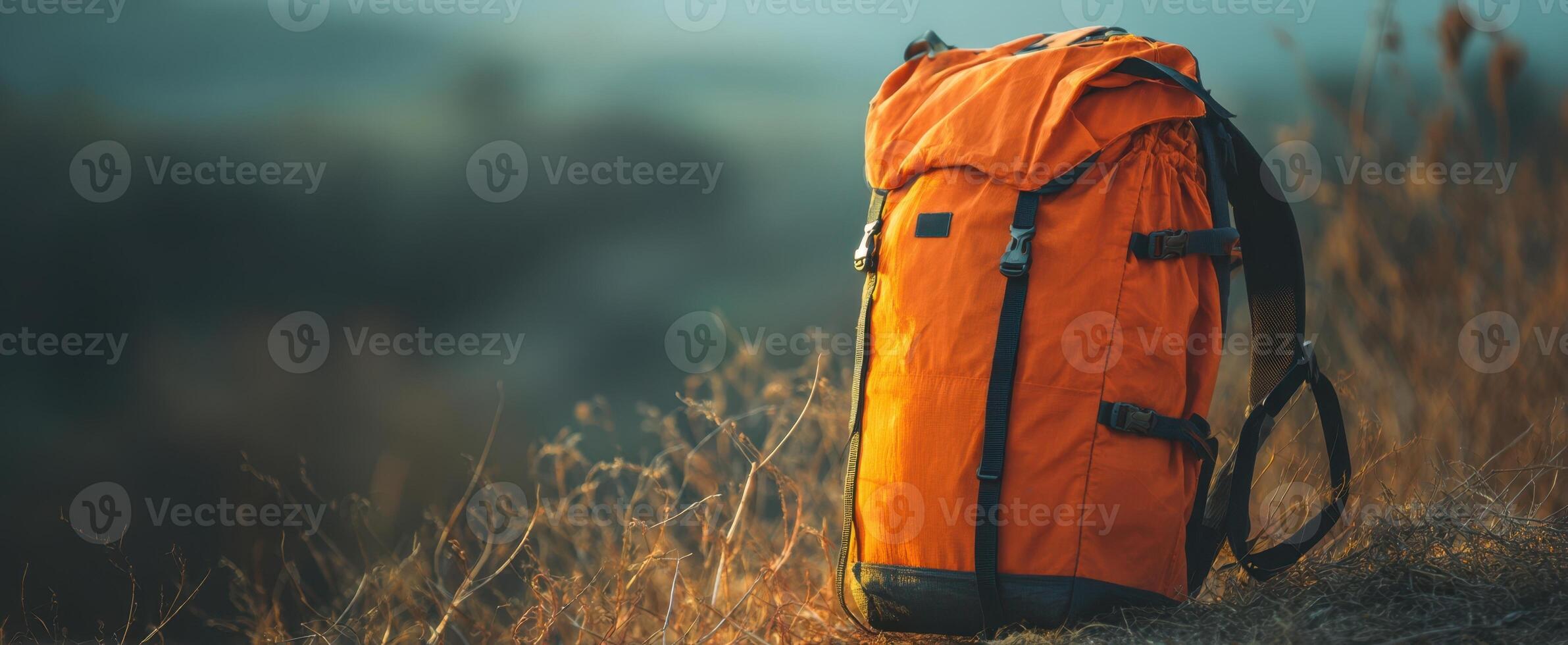 The vibrant orange backpack resting on a grassy hillside in nature. photo
