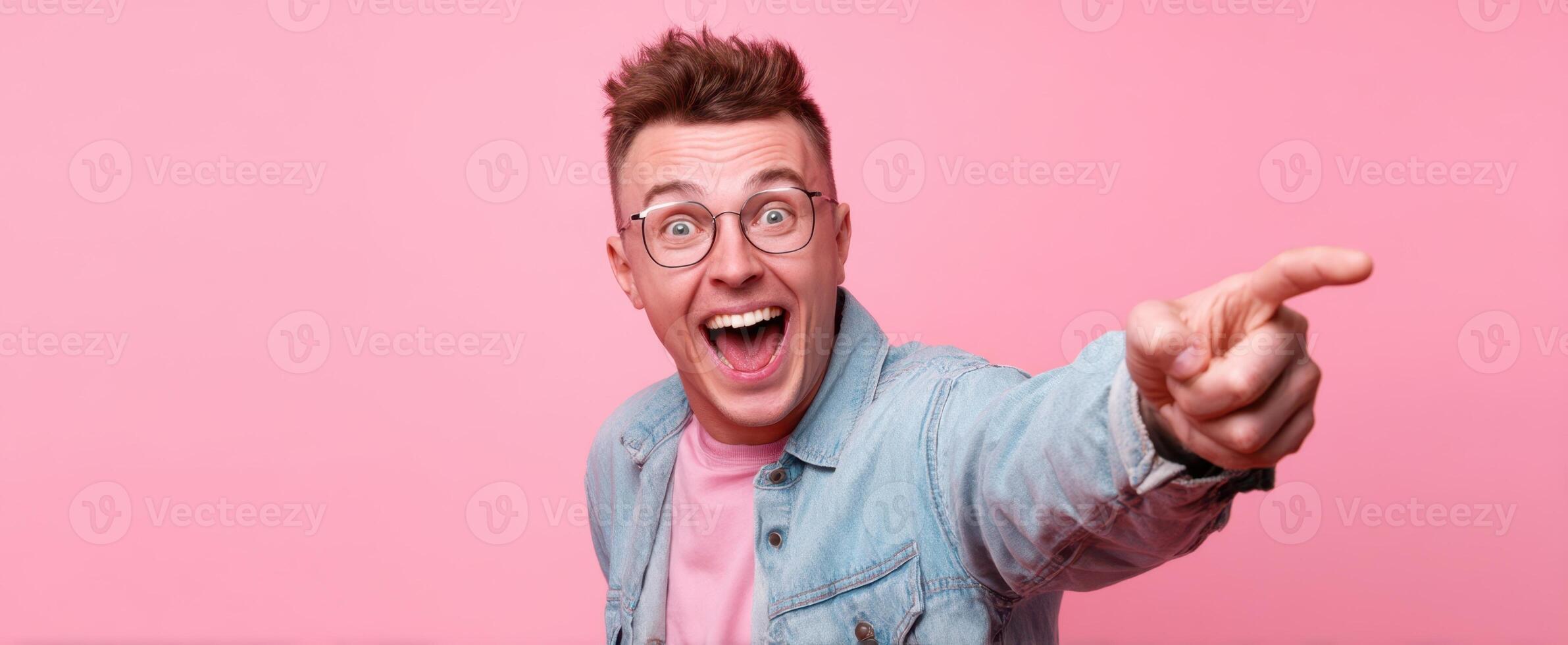 The cheerful young man joyfully pointing at something exciting in a pink setting. photo