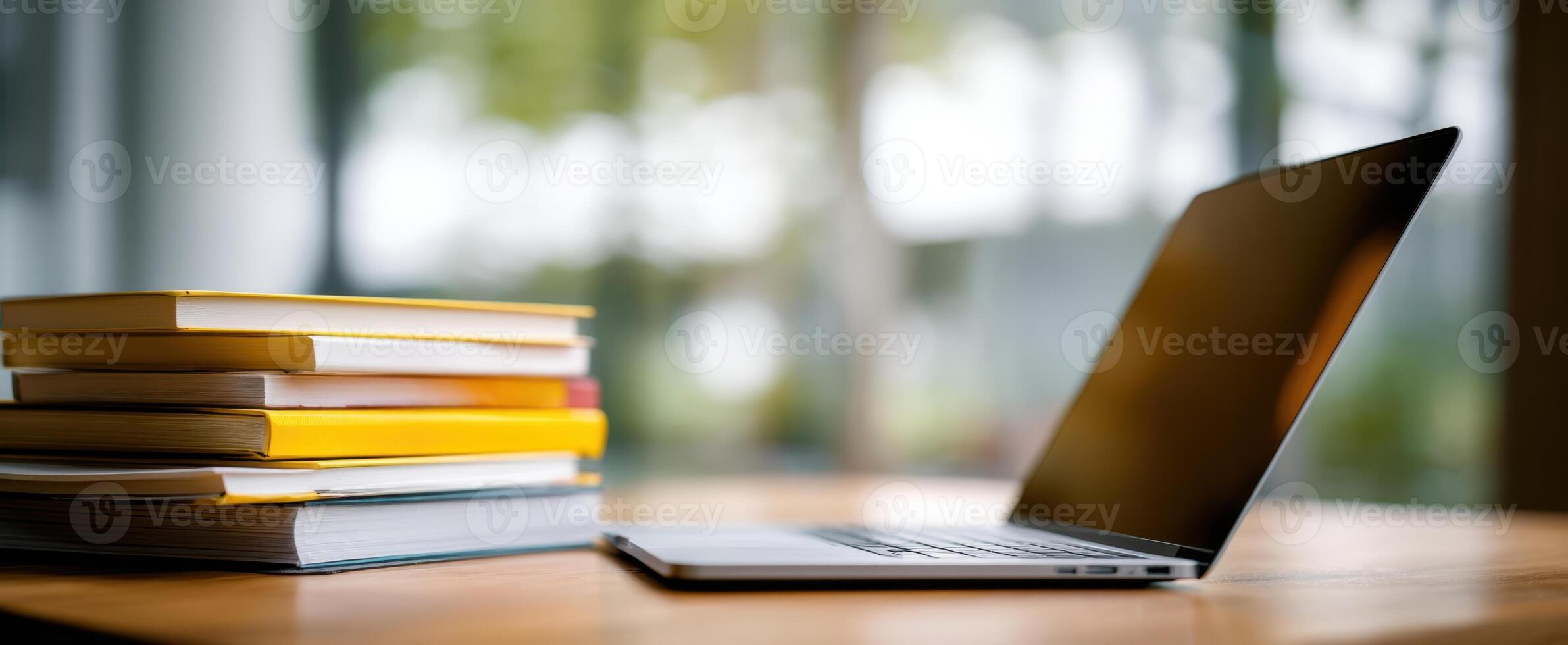 The sleek laptop placed beside a stack of colorful books on a wooden desk. photo