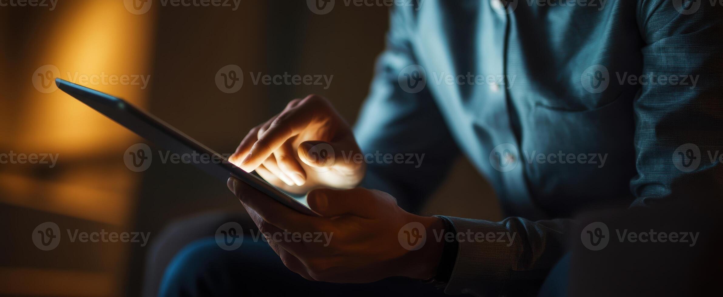 The individual using a tablet in a cozy, dimly lit environment. photo
