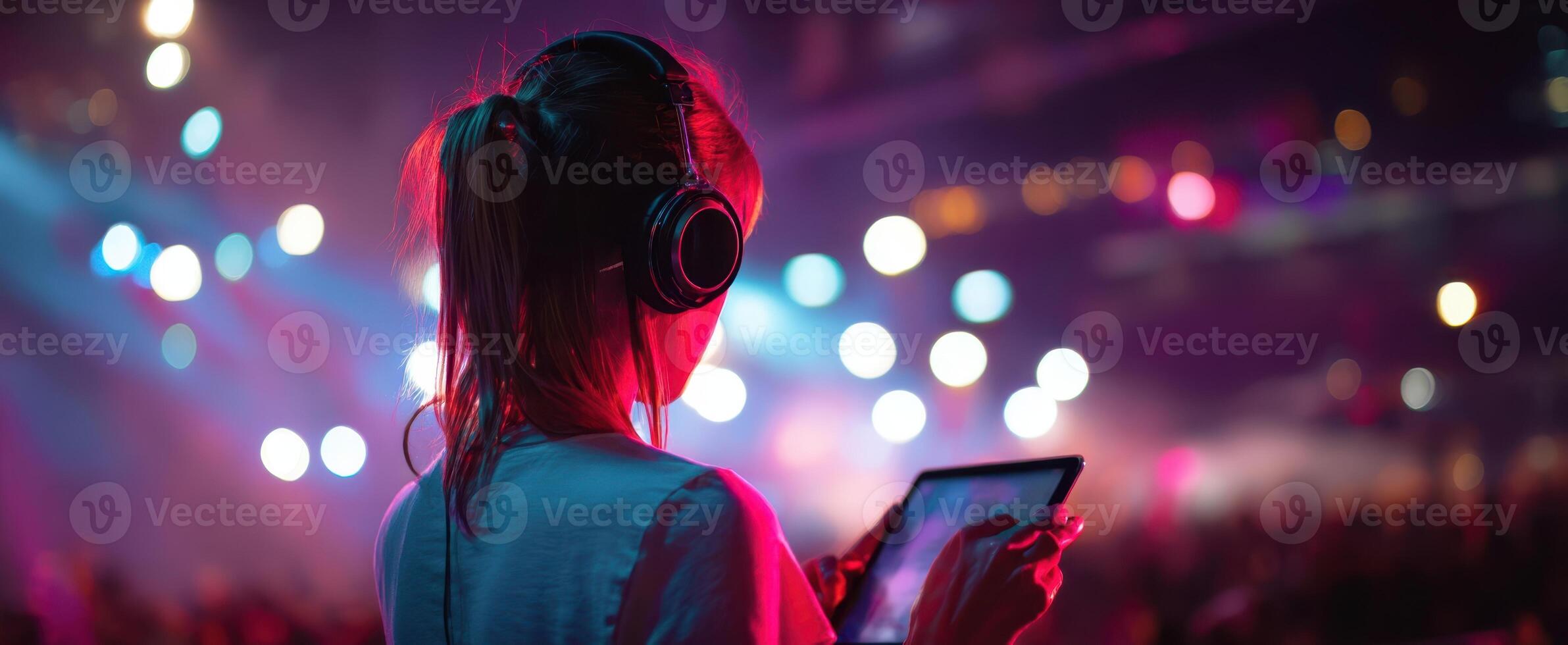 The young woman enjoying music at a vibrant concert with headphones and tablet. photo