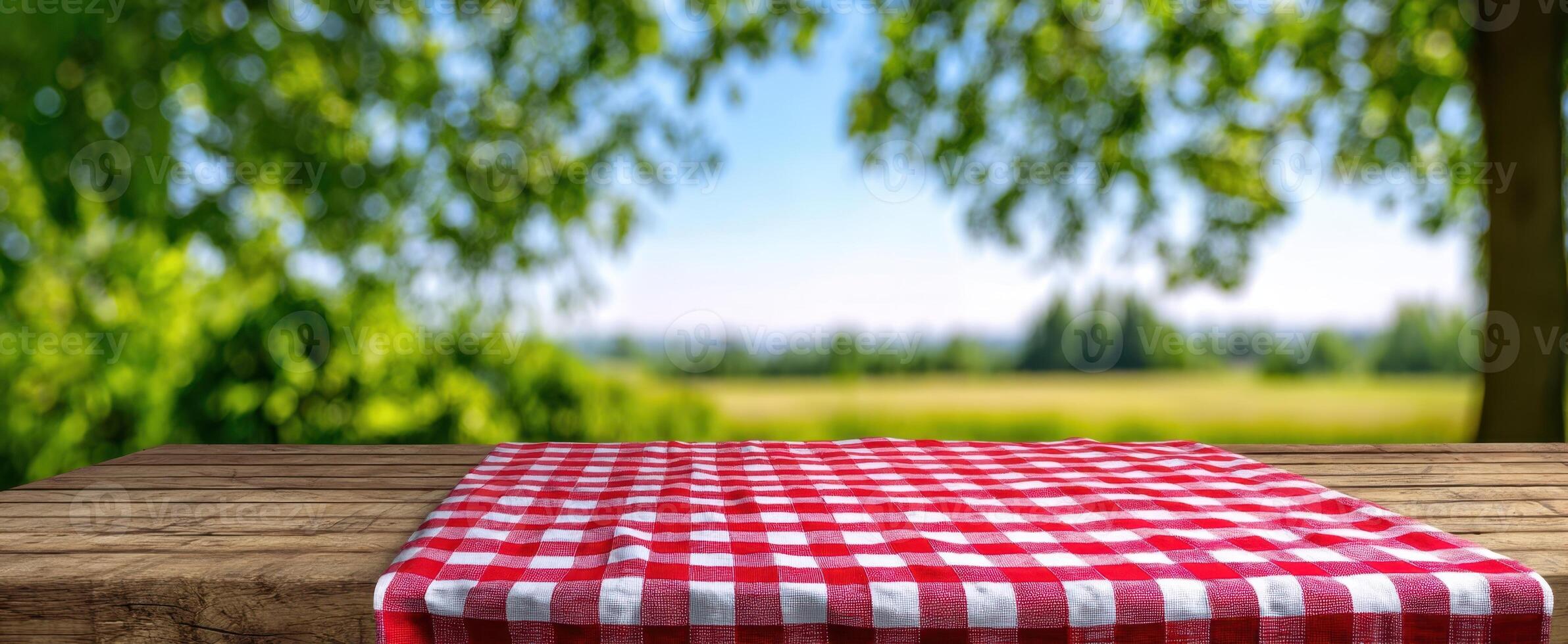 The red checkered picnic blanket on a rustic wooden table in a lush outdoor setting. photo