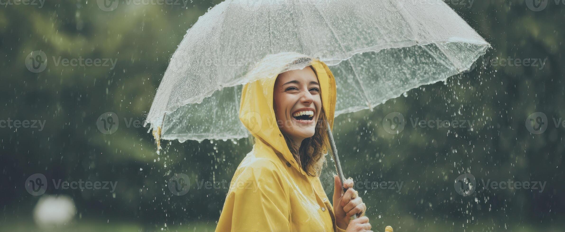 The joyful woman in a yellow raincoat holding a transparent umbrella outdoors. photo