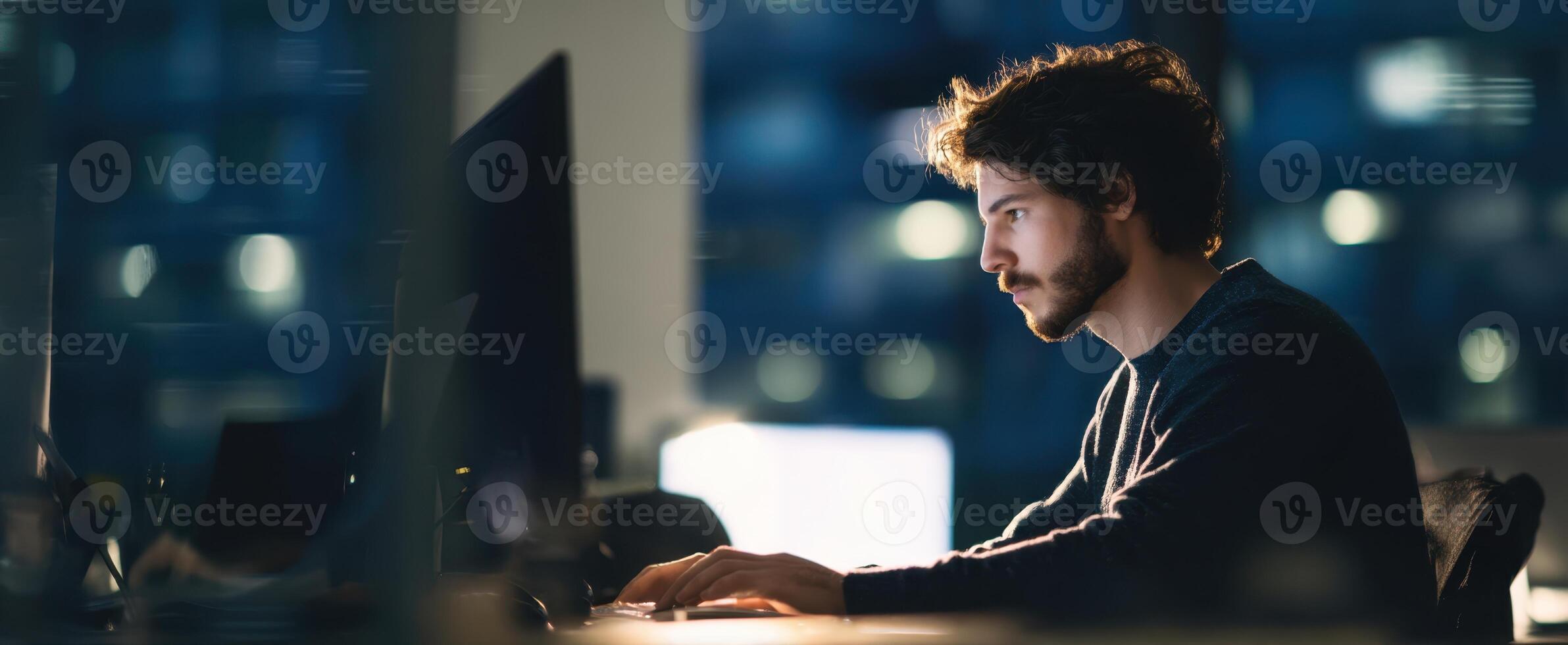 The focused man working on a computer in a modern office at night. photo