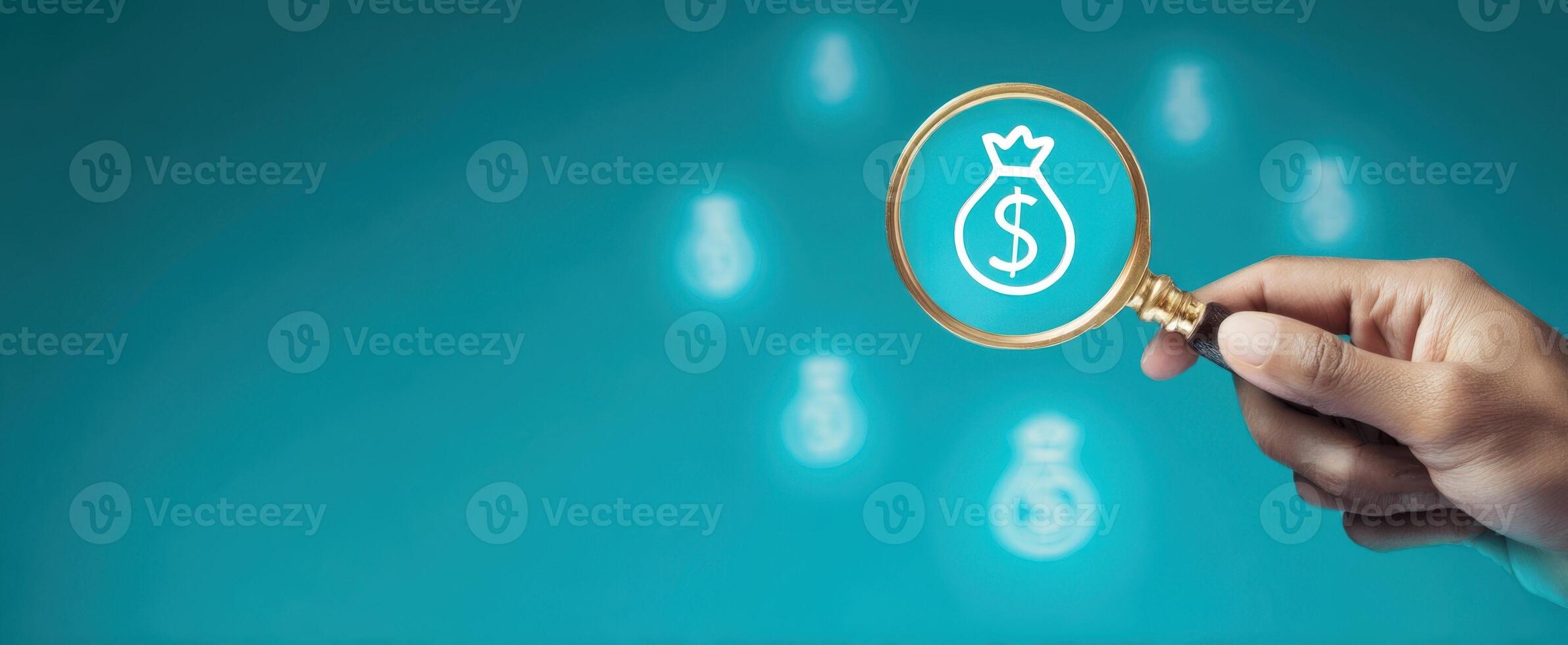 The hand holding a magnifying glass over money symbols on a turquoise background. photo