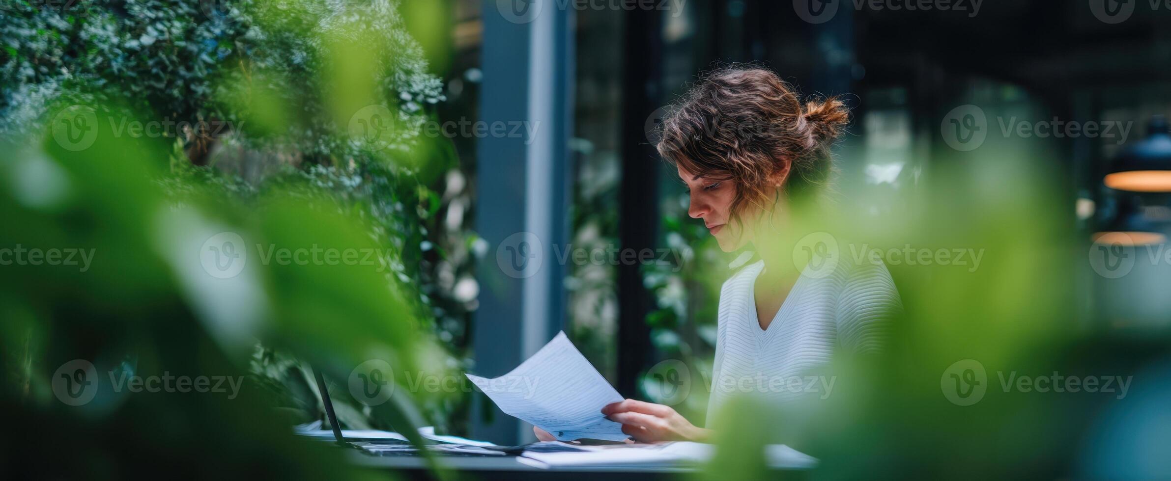 The woman reading documents in a lush green workspace surrounded by plants. photo